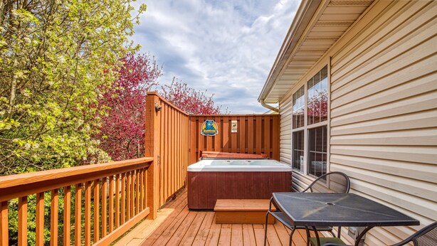 A wooden deck with a hot tub, a table, and chairs, and a sign indicating a dog-friendly area.