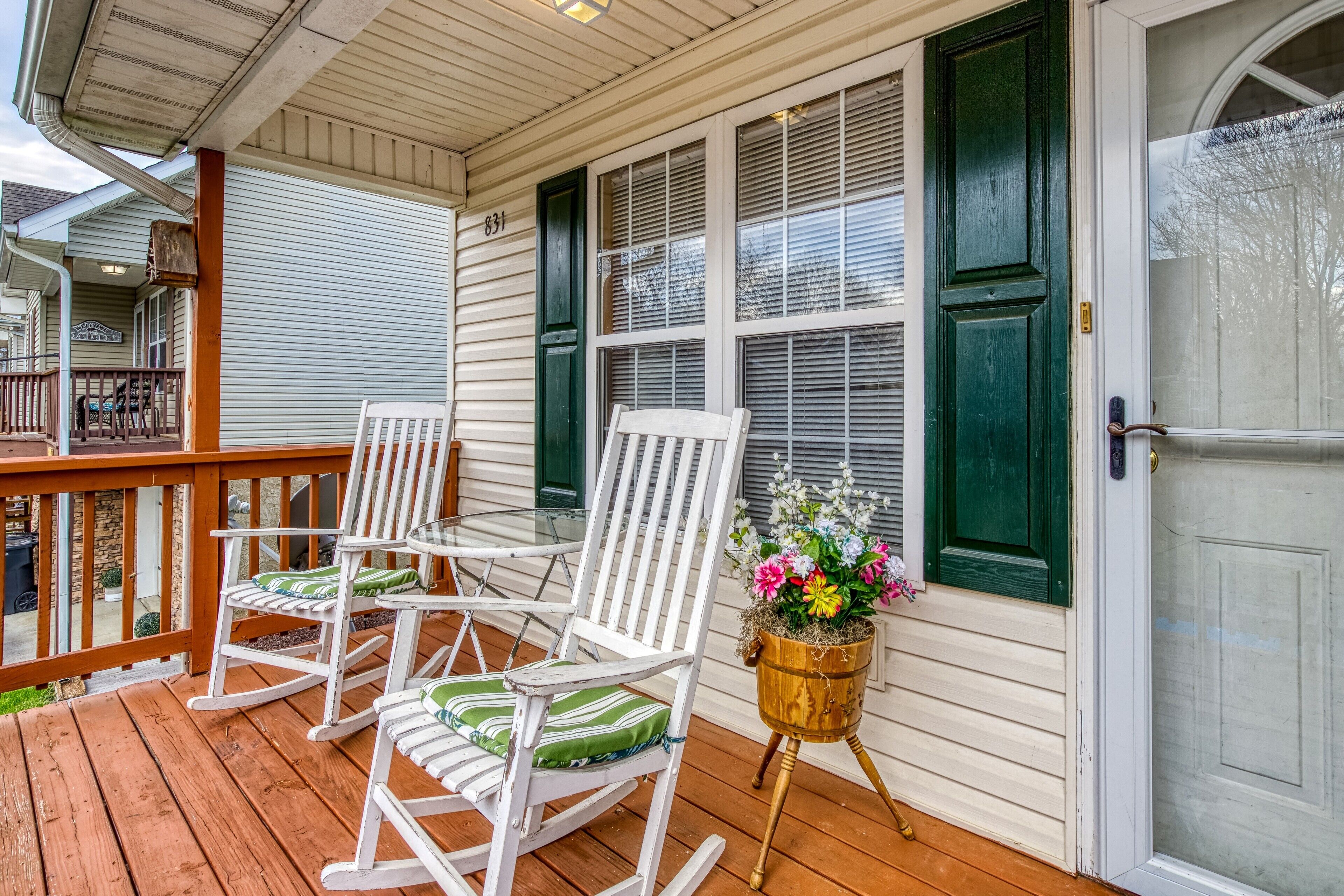 A porch with three white rocking chairs and a wooden planter with flowers.