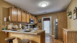 A kitchen with wooden cabinets, a central island with stools, a microwave, and a refrigerator.