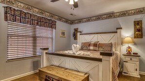 A bedroom with a bed, a nightstand, a lamp, a wooden chest, and a window with blinds.