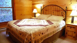 A wooden cabin bedroom with a bed, two bedside lamps, and a window with a view of trees. - Dreamcatcher-Harvest Moon Cottages (Rockbridge)