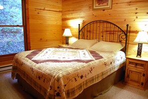 Een houten slaapkamer met een bed, twee bedlampen en een raam met uitzicht op bomen.