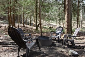 Een camping met Adirondack-stoelen rond een vuurkuil, gelegen in een bebost gebied.