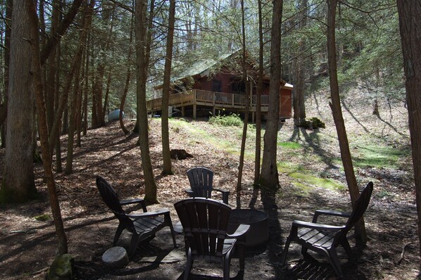 A cabin in a forest with a deck and outdoor seating area.