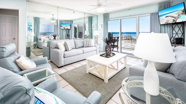 Un salon moderne avec un canapé gris, une table basse en verre et une vue sur la plage grâce à de grandes fenêtres.