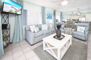 A living room with a grey sofa, a white coffee table, and a TV mounted on the wall. - Gulf Dunes 217 • Beautiful 3BR 3BA Beachfront Corner Unit, Direct Ocean View, Free Beach Service (Fort Walton Beach)
