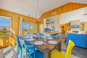 A dining area with a wooden table set for six, a kitchen in the background, and a living area with a blue sofa.