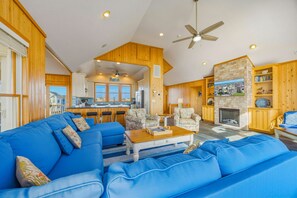A spacious living room with a blue sofa set, a fireplace, and a kitchen area visible through an open doorway.