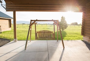 A wooden swing set under a covered area with a view of a grassy field and distant buildings.