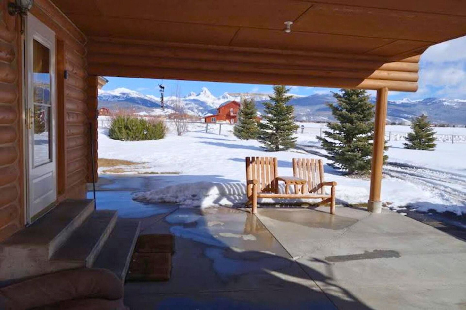 Une cabane en bois dotée d’un porche abrité, d’un banc et offrant une vue sur des montagnes enneigées.
