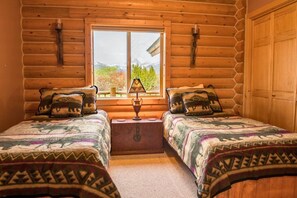 A log cabin bedroom with two beds, a window, and a lamp.