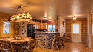 A cozy cabin interior with a stone island in the center, wooden dining table, and chairs. - Gorgeous Saddlehorn Cabin - Amazing Teton Views (Driggs)