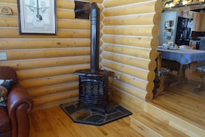 Ein rustikales Holzhütten-Interieur mit Holzofen, einem gerahmten Bild an der Wand und einem Essbereich mit Tisch und Stühlen.