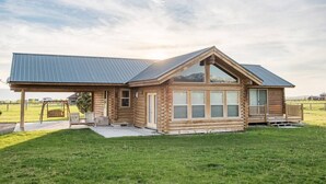 A log cabin with a large porch, a swing set, and a view of the surrounding landscape. - Gorgeous Saddlehorn Cabin - Amazing Teton Views (Driggs)