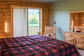 Une chambre aménagée dans un chalet en rondins, comprenant un lit, une chaise, une commode et une porte-fenêtre coulissante donnant sur une terrasse extérieure.