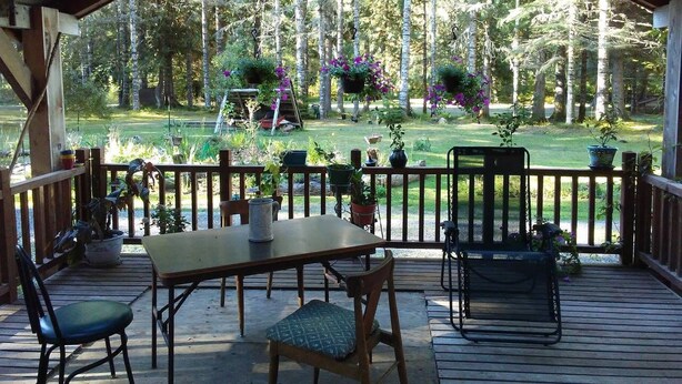 Une terrasse extérieure couverte, avec une table et des chaises en bois, entourée d’une balustrade en bois.
