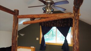 Une chambre avec un plafond en pente, un ventilateur de plafond, une fenêtre avec des rideaux et un lit avec une tête de lit.