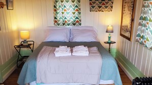 A neatly made bed with pillows and folded towels, a wooden floor, a patterned rug, and a small table with a lamp. - Kims Cozy Rustic Cabin 5 min. from Cody (Cody)