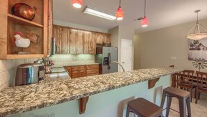 Una cocina con gabinetes de madera, encimeras de granito e iluminación colgante.