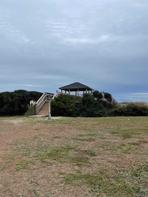 A gazebo with a roof and a staircase leading up to it, surrounded by grass and bushes.