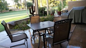 Un patio al aire libre con una mesa y sillas, rodeado de plantas en macetas y vistas a un jardín.