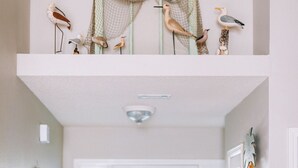 A hallway with a white door, a small table, and a shelf with decorative items. - 5 Bedroom/3 Bath Emerald Coast Beach Cottage in gated resort community (Destin)