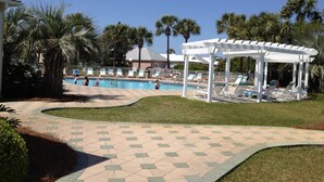 A pool area with a covered seating area, palm trees, and a clear blue sky. - 5 Bedroom/3 Bath Emerald Coast Beach Cottage in gated resort community (Destin)