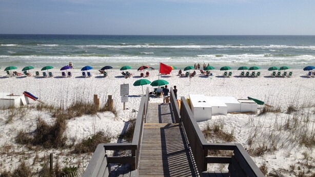 A beach with a wooden boardwalk leading to the shore, lined with beach chairs and umbrellas. - 5 Bedroom/3 Bath Emerald Coast Beach Cottage in gated resort community (Destin)