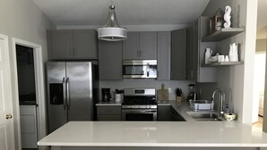 A modern kitchen with grey cabinets, stainless steel appliances, a central island, and a hanging light fixture. - 5 Bedroom/3 Bath Emerald Coast Beach Cottage in gated resort community (Destin)