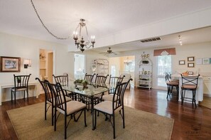 Un comedor con una mesa de vidrio rodeada de sillas, un candelabro y un ventilador de techo.