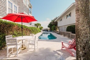 Una piscina con un paraguas rojo, sillas blancas y una mesa en un entorno residencial.