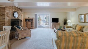 A living room with a brick fireplace, a television, a sofa, and a dining area with chairs. - 47 Dune Lane - My Sunshine, Oceanfront 5 Bedroom, North Forest Beach (Hilton Head Island)