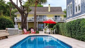 A swimming pool with a red umbrella, white deck chairs, and a two-story building with balconies. - 47 Dune Lane - My Sunshine, Oceanfront 5 Bedroom, North Forest Beach (Hilton Head Island)