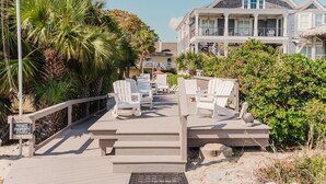 A private property with a wooden deck, white chairs, and a building with a balcony.