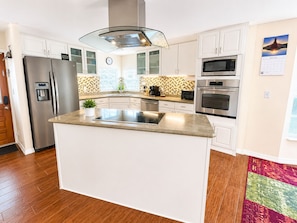 A modern kitchen with white cabinets, a stainless steel refrigerator, a microwave, an oven, and a glass-top island.