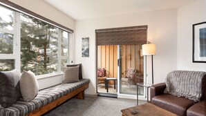 A cozy living room with a bench, a sofa, and a coffee table. There is a door leading to a balcony with chairs and a table. - Mountain Views in Whistler Village (Whistler)