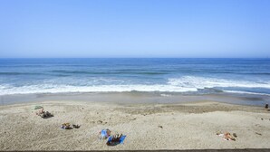 A beach with a clear sky, calm sea, and a few beachgoers.