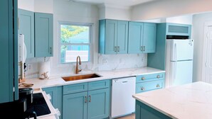 A modern kitchen with teal cabinetry, white countertops, and a built-in dishwasher.
