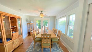 A dining area with a long wooden table, chairs, a ceiling fan, and a large window.