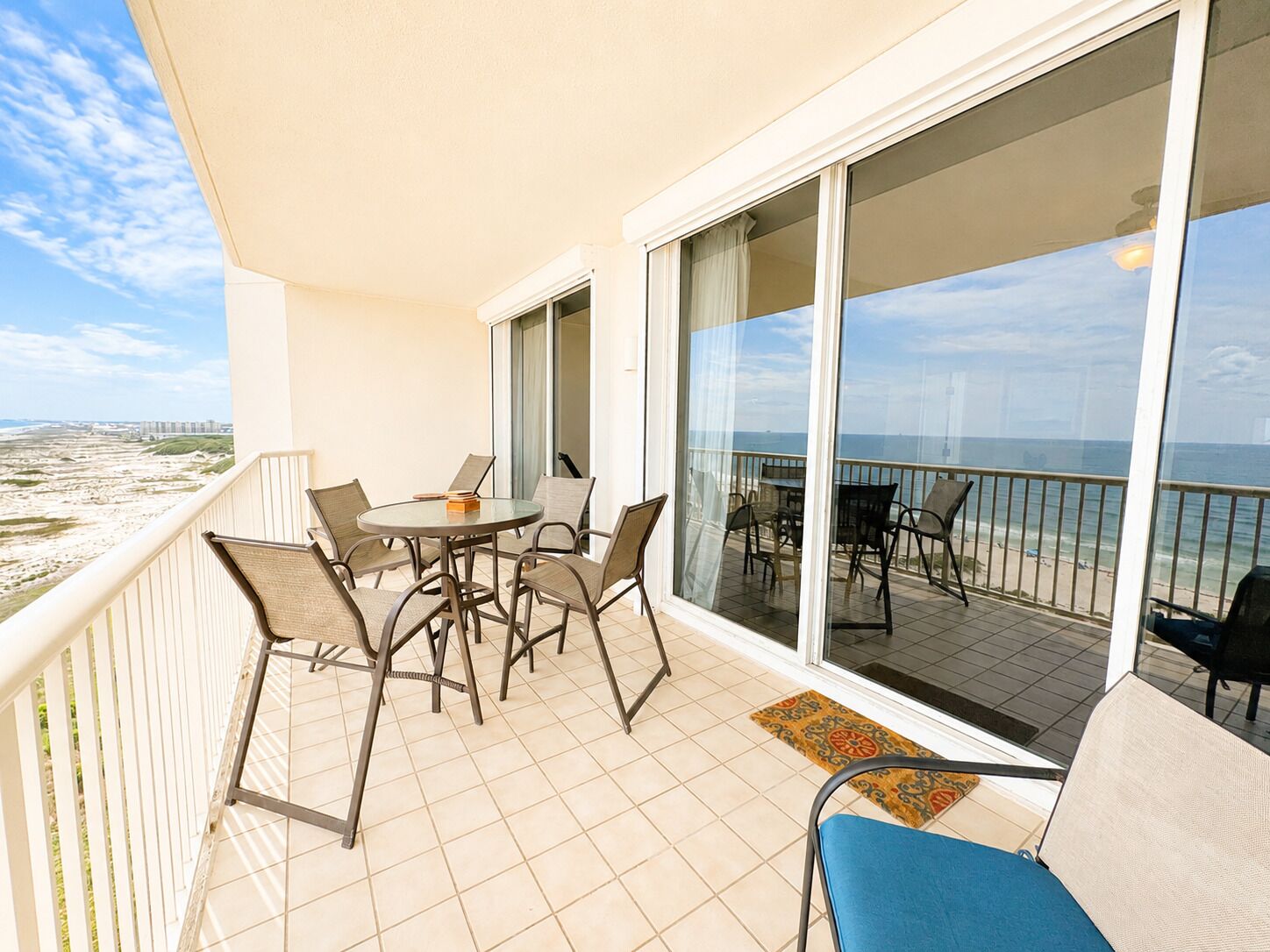 Een balkon met een tafel en stoelen, grote schuiframen en uitzicht op het strand.