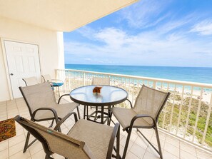 Ein Balkon mit rundem Tisch und vier Stühlen mit Blick auf einen Strand.