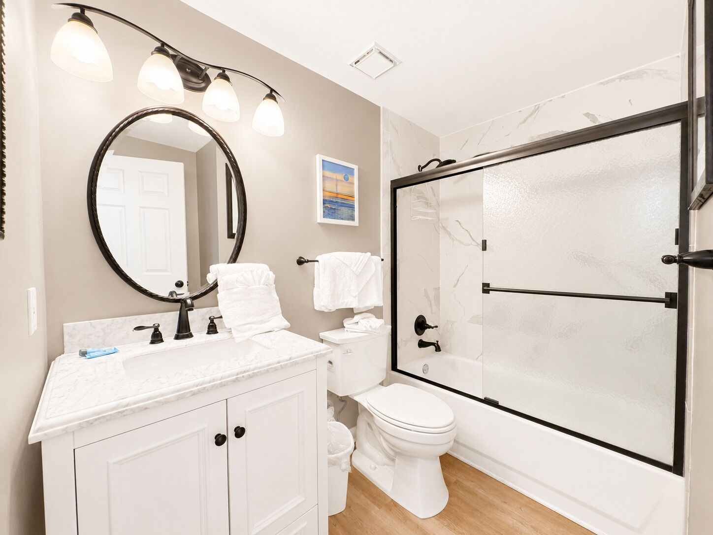 A bathroom with a white vanity, a round mirror, a toilet, and a glass-enclosed shower.