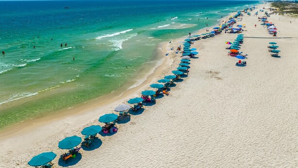 Una playa con hileras de sombrillas y sillas, una orilla arenosa y el océano.