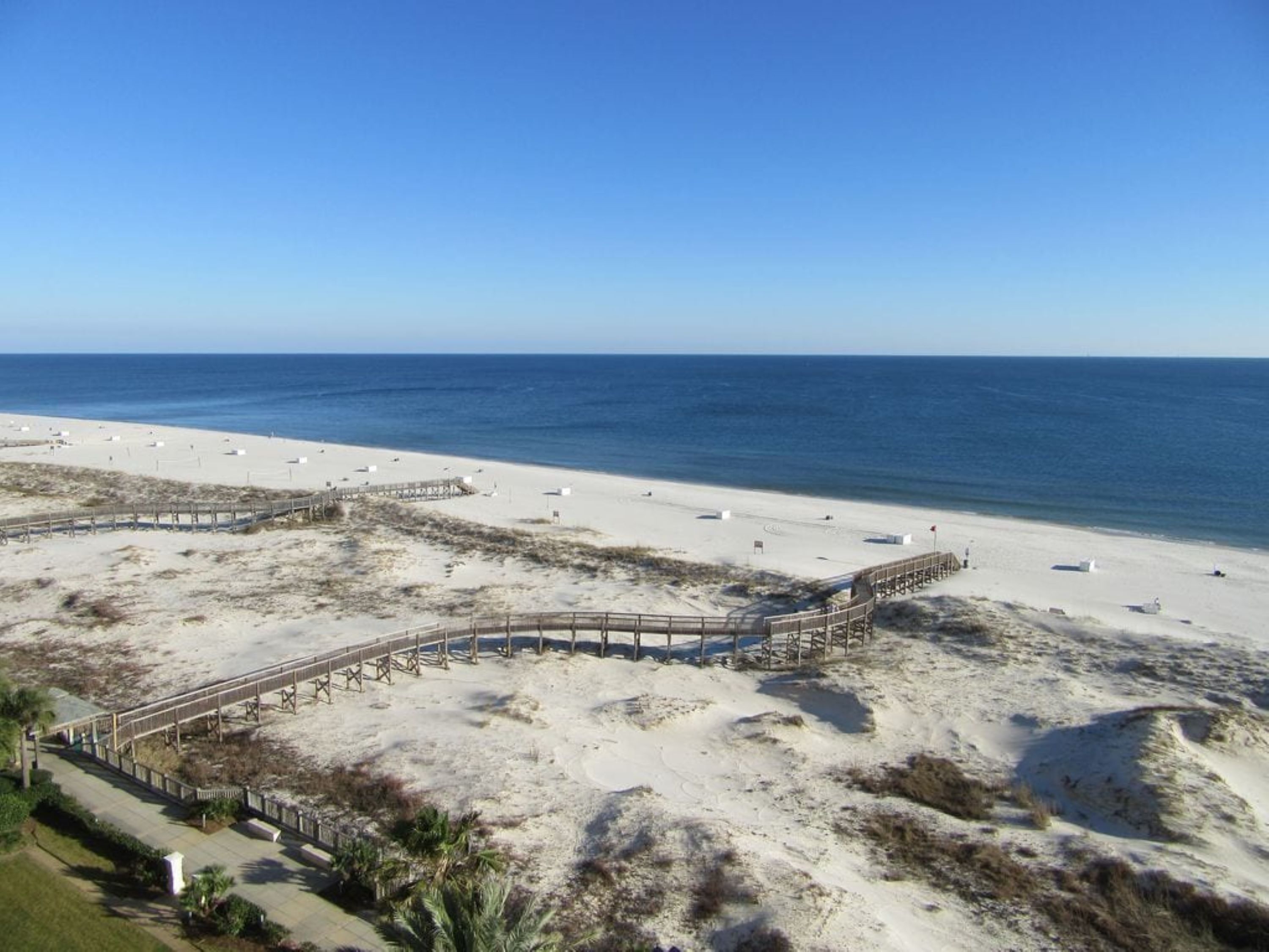 A beach with a wooden boardwalk and white beach umbrellas.