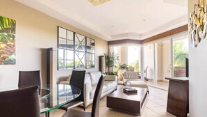 A modern living room with a glass dining table, leather chairs, a sofa, and a coffee table. There is a large abstract painting on the wall and a potted plant in the corner. - Ocean view w/ pool, rooftop & beach (Playa Langosta)