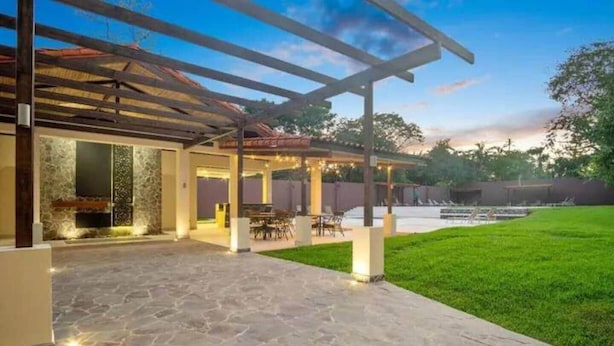 A covered outdoor patio area with stone flooring, a seating arrangement, and a view of a swimming pool. - Ocean view w/ pool, rooftop & beach (Playa Langosta)