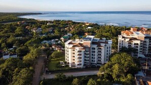 A high-rise building with multiple floors, surrounded by greenery and a view of the sea. - Ocean view w/ pool, rooftop & beach (Playa Langosta)