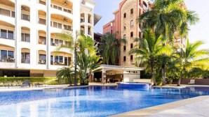 A hotel with a large swimming pool, palm trees, and a covered area. - Ocean view w/ pool, rooftop & beach (Playa Langosta)