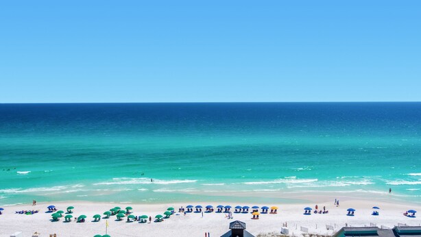 A beach with white sand, clear turquoise water, and a row of umbrellas.
