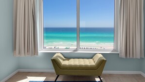 A room with a large window overlooking a beach, a beige sofa, and light blue walls.